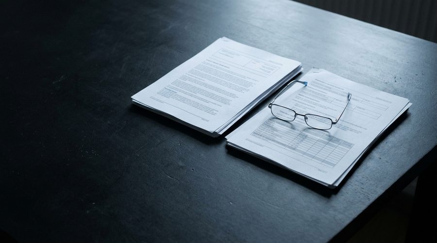 Zwei Angebotsunterlagen mit Lesebrille auf einem dunklen Tisch